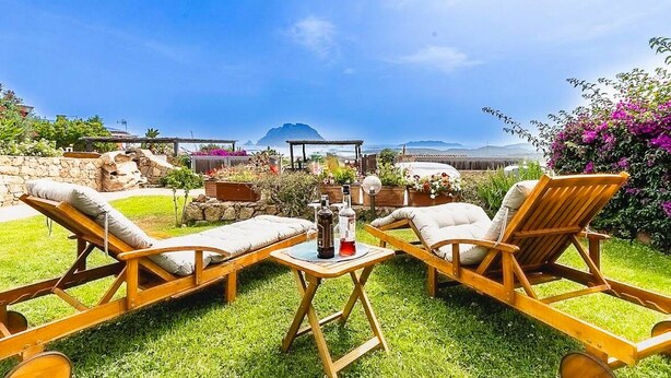 Une terrasse dotée de chaises longues en bois et d’une table, offrant une vue panoramique sur l’océan et les montagnes.