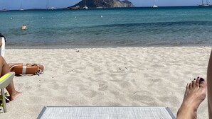 Une plage avec un ciel dégagé, un rivage sablonneux et une île rocheuse à l’horizon.