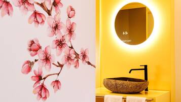 A bathroom with a stone sink, a round mirror, and a wall with cherry blossom artwork.