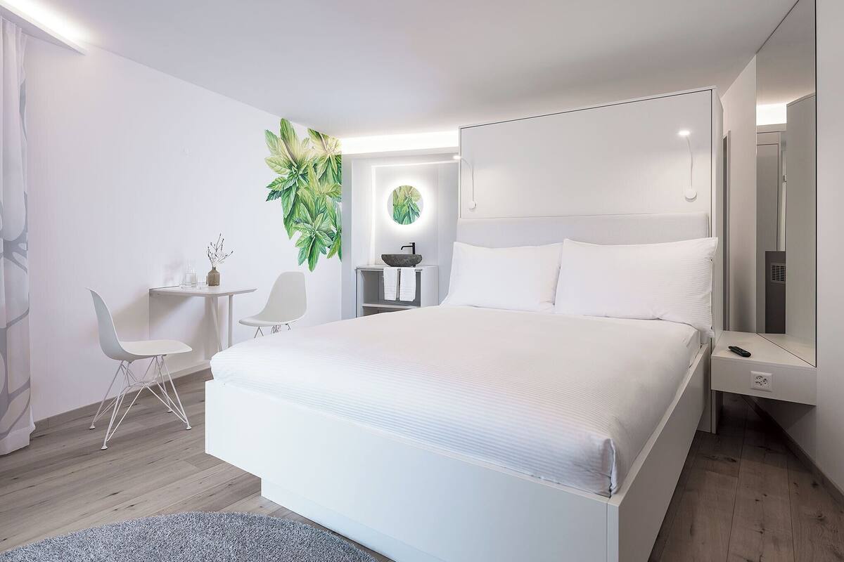 A modern hotel room with a large bed, a desk, and a chair.