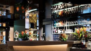 A bar area with a marble countertop, bar stools, and shelves stocked with bottles and glasses. - Neuro Campus Hotel by CERENEO PREVENTION (Vitznau)