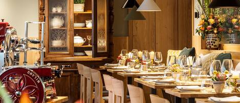 A restaurant with wooden tables and chairs, a large cabinet with glass doors, and pendant lights.