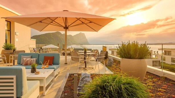 A rooftop terrace with outdoor seating, a large umbrella, and a view of the sea and mountains. - Neuro Campus Hotel by CERENEO PREVENTION (Vitznau)