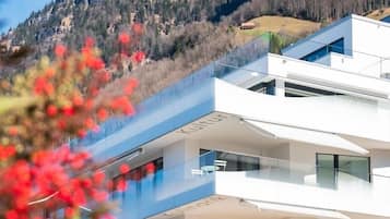 Un edificio moderno de varios pisos con balcones y ventanas amplias, con montañas al fondo.