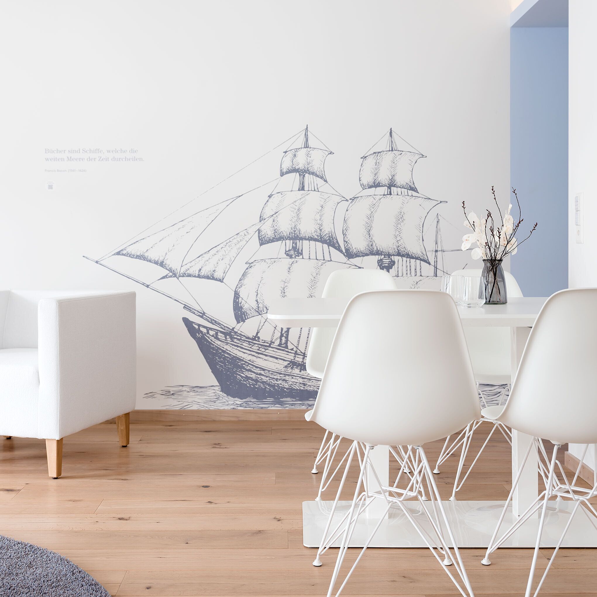Una sala de estar moderna con un gran mural de un barco velero, muebles blancos y un jarrón con ramas.