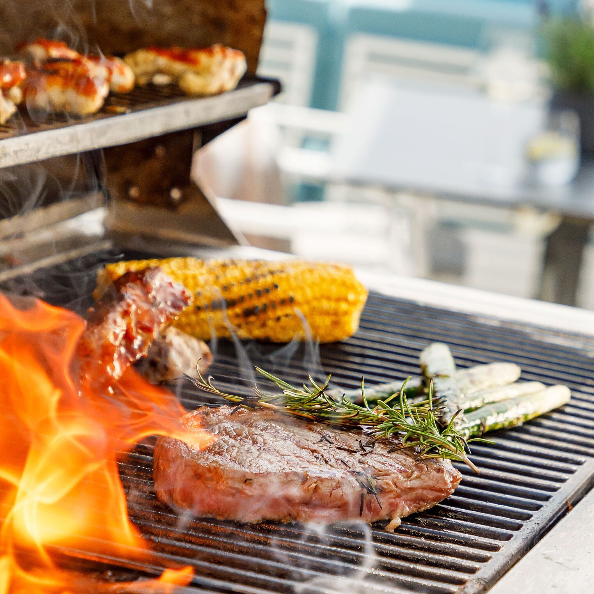 Un barbecue avec un steak, des épis de maïs et des légumes en train de cuire.