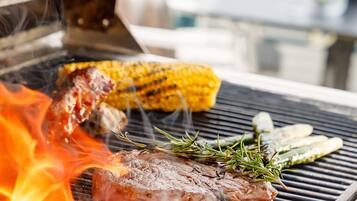 Un barbecue avec un steak, des épis de maïs et des légumes en train de cuire.