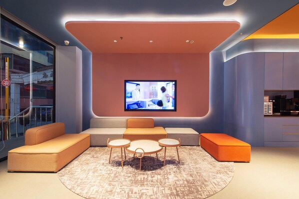 A modern lounge area with a flat-screen TV, seating, and a patterned rug.