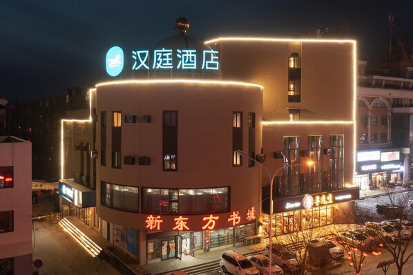 A hotel with a prominent sign, a modern facade, and a parking area.