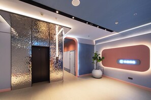 A modern lobby with a metallic wall feature, a reception desk, and a potted plant.