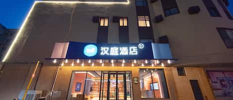 A hotel entrance with illuminated signage, a glass door, and a visible interior with seating and a counter.
