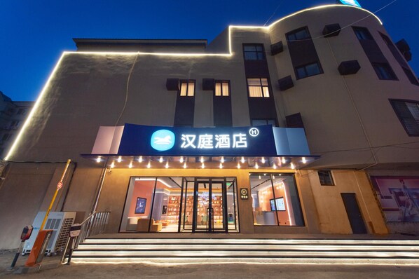 A hotel entrance with illuminated signage, a glass door, and a visible interior with seating and a counter.
