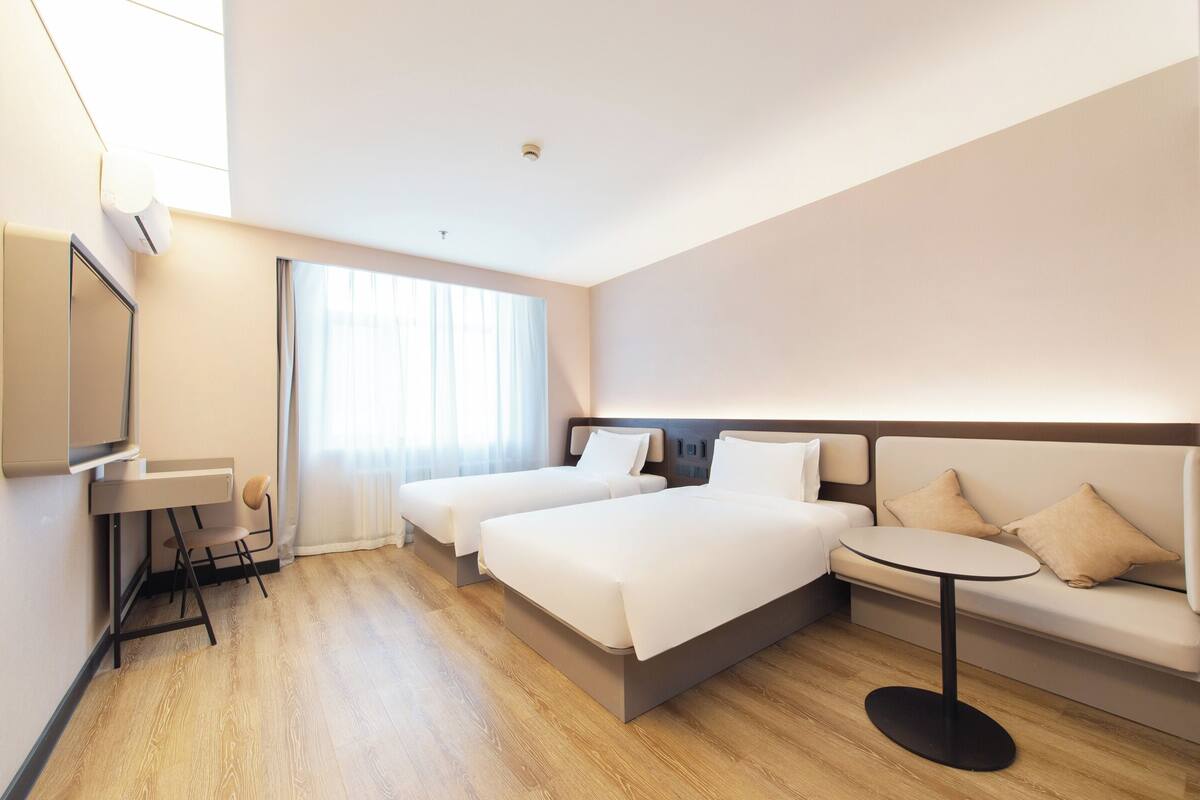 Habitación de hotel con dos camas, un sofá, una mesita, un televisor y una ventana con cortinas.