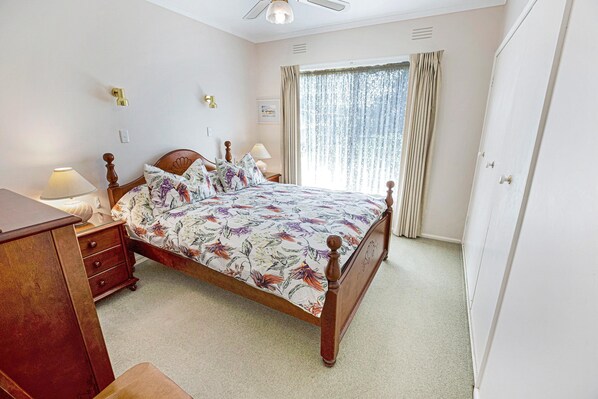 Een slaapkamer met een houten bed, een nachtkastje, een lamp en een raam met gordijnen.
