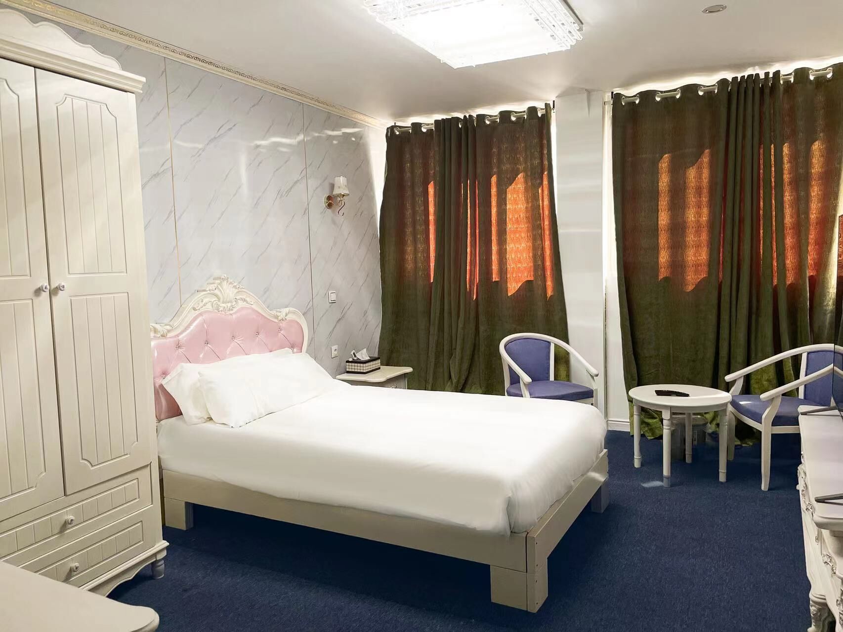 Une chambre d’hôtel avec un lit, une armoire, une petite table avec des chaises et une fenêtre avec des rideaux.