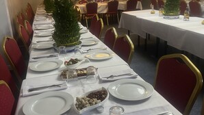 Una larga mesa de comedor dispuesta para un evento formal, con manteles blancos, sillas rojas y vajilla y cubertería ordenadas.