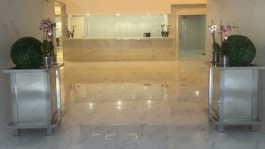 Un vestíbulo moderno con piso de mármol, un mostrador de recepción y plantas decorativas.