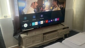 Un televisor sobre un mueble de madera en una habitación de hotel, con cama y cortinas.