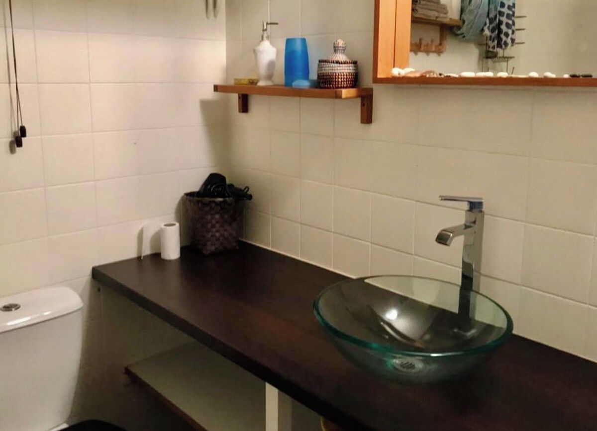 Ein Badezimmer mit einem Waschbecken aus Glas, einer Toilette und einem Regal mit dekorativen Objekten.