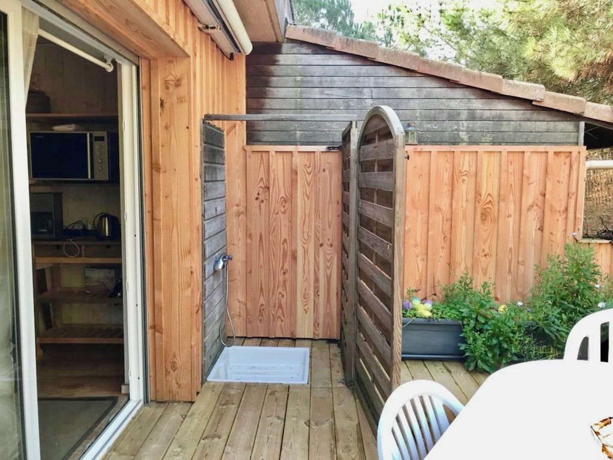 A wooden deck with a sliding door leading to a kitchen area, a small outdoor seating area, and a wooden fence.