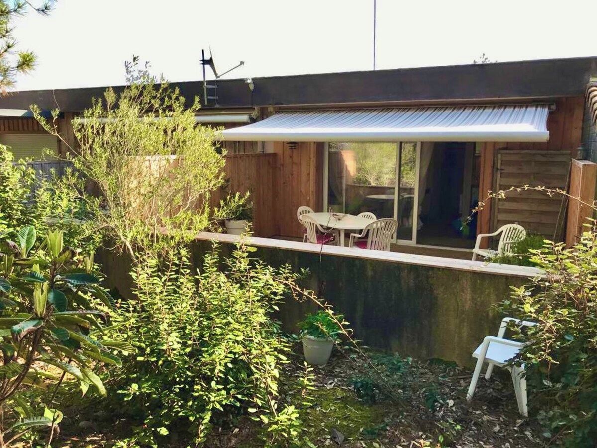 Una casa de fusta amb terrassa coberta, una taula petita i cadires.