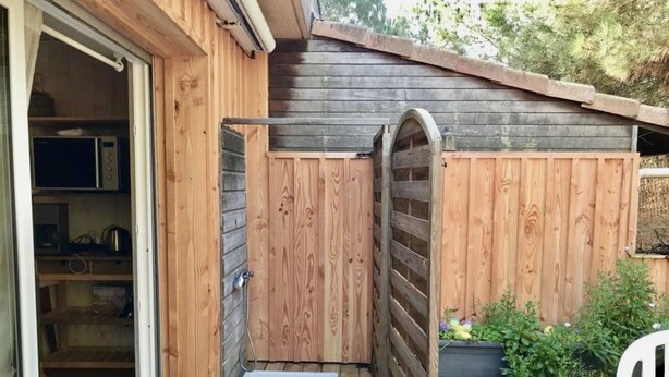 Eine Holzterrasse mit einer Schiebetür, die zu einer Garage führt, einem kleinen Sitzbereich im Freien und einem Blumenbeet mit Pflanzen.