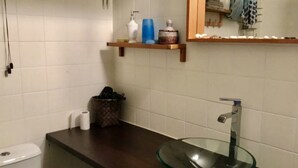 Ein Badezimmer mit einem Waschbecken aus Glas, einer Toilette, einem Ablagefach für Toilettenartikel und einem Spiegel.