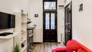 A living room with a red sofa, a black TV on a stand, and a small table with a plant. There is a door leading to another room and a radiator on the wall. - Real Apartments Klauzal II (Budapest)