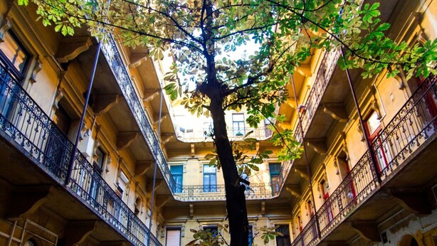 A courtyard with a tree in the center, surrounded by multi-story buildings with balconies and railings. - Real Apartments Klauzal II (Budapest)