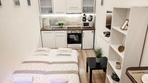 A compact hotel room with a bed, a small desk, a kitchenette, and a bookshelf. - Real Apartments Klauzal II (Budapest)