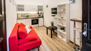 A compact living space with a kitchenette, a sofa with red cushions, a small table with a plant, and a TV mounted on the wall. - Real Apartments Klauzal II (Budapest)