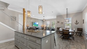 Een ruime keuken met een groot eiland, een houten eettafel en moderne hanglampen.