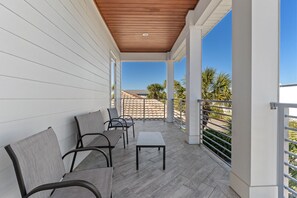 Un balcón techado con techo de madera, paredes blancas y vista a una zona residencial con palmeras.