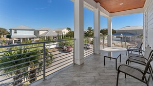 Een overdekt balkon met uitzicht op omliggende huizen, een verhard terras en enkele geparkeerde auto's.