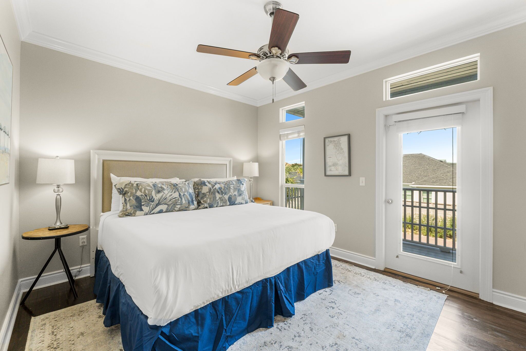 A bedroom with a large bed, a ceiling fan, a nightstand, a lamp, and a view of the outdoors through a door.