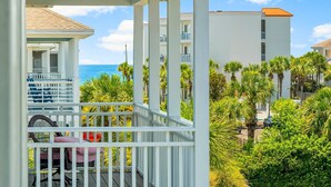 Un balcon avec vue sur l’océan, des palmiers et un immeuble doté de balcons.