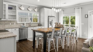 Une cuisine moderne avec des meubles blancs, un îlot central en bois et un coin repas doté de chaises en métal.