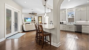A modern kitchen with white cabinets, a central island, and a dining area with chairs. - Walk to Beach ~ Gated Community ~ Gourmet Kitchen (Destin)