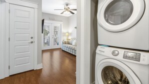 A laundry room with stacked washers and dryers, a door leading to a living area with a ceiling fan, and a view of a backyard through a glass door. - Family Friendly ~ Gated Community ~ Lagoon Pool (Destin)