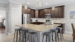 A modern kitchen with dark wood cabinets, stainless steel appliances, granite countertops, and bar stools. - Family Friendly ~ Gated Community ~ Lagoon Pool (Destin)