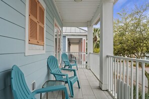 A porch with teal Adirondack chairs, a white railing, and a view of a residential street.