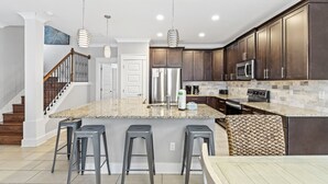 A modern kitchen with dark wood cabinets, stainless steel appliances, a granite countertop, and a central island with bar stools. - Family Friendly ~ Gated Community ~ Lagoon Pool (Destin)