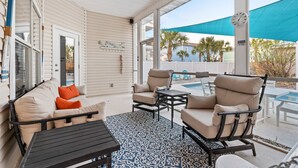 Eine überdachte Terrasse mit Pool, beiger und orangefarbener Möbel sowie einem blau gemusterten Teppich.