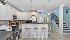 A modern kitchen with white cabinets, a stainless steel refrigerator, and a bar area with stools. - Gated Community ~ Lagoon Pool ~ Golf Cart (Destin)