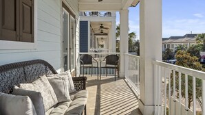 A covered porch with a sofa and chairs, a ceiling fan, and a view of the street and buildings in the background. - Gated Community ~ Lagoon Pool ~ Golf Cart (Destin)