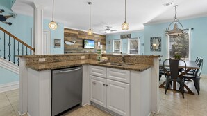 A kitchen with granite countertops, white cabinets, and a dishwasher. There is a dining area with a table and chairs. - Gated Community ~ Lagoon Pool ~ Golf Cart (Destin)