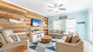A living room with a wooden wall, a ceiling fan, a TV, a sofa, a coffee table, and a rug. - Gated Community ~ Lagoon Pool ~ Golf Cart (Destin)
