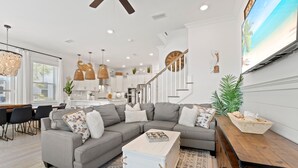 A modern living room with a sectional sofa, a coffee table, and a dining area with chairs and a table. - 30A Prominence ~ Golf Cart 6-Seat ~ Community Pool (Panama City Beach)