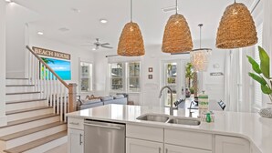 A modern kitchen with white cabinetry, a large island with a sink, and hanging wicker pendant lights. - 30A Prominence ~ Golf Cart 6-Seat ~ Community Pool (Panama City Beach)