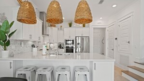 A modern kitchen with white cabinetry, stainless steel appliances, and a large island with bar stools. - 30A Prominence ~ Golf Cart 6-Seat ~ Community Pool (Panama City Beach)